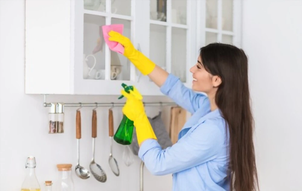 smiling woman wearing protective rubber gloves cleaning painted cabinets surface